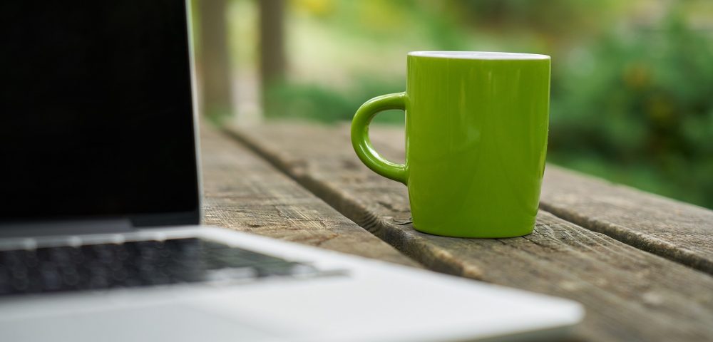 Imagen en primer plano de una taza verde al lado de un ordenador portátil